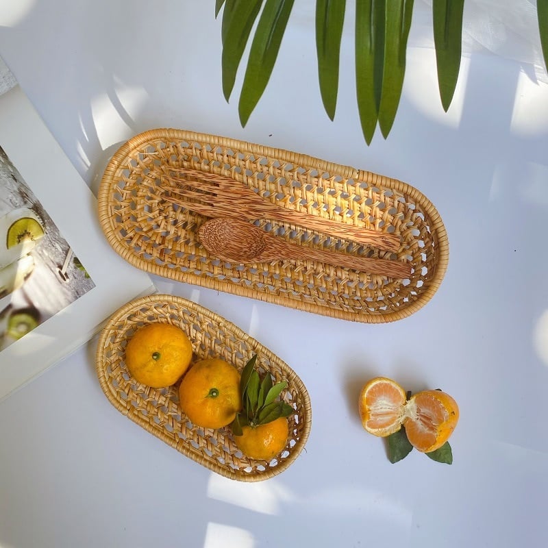 Two oval woven rattan baskets holding oranges and wooden utensils
