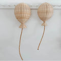 Two hand woven rattan balloons with trailing strings hanging on a wall