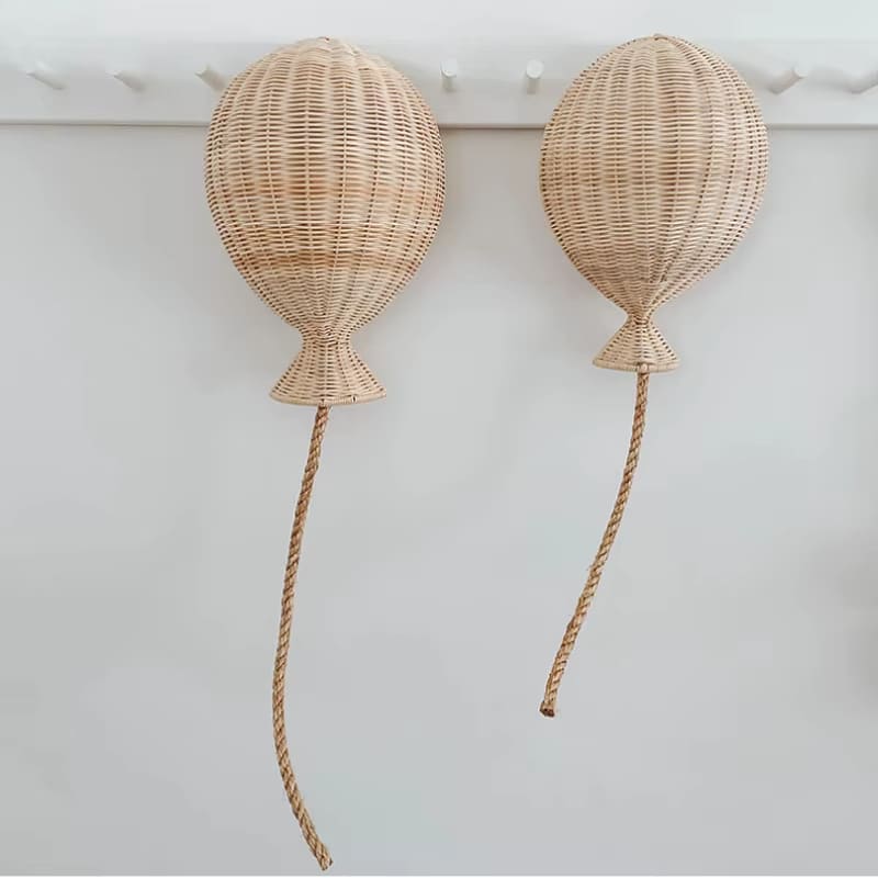 Two hand woven rattan balloons with trailing strings hanging on a wall