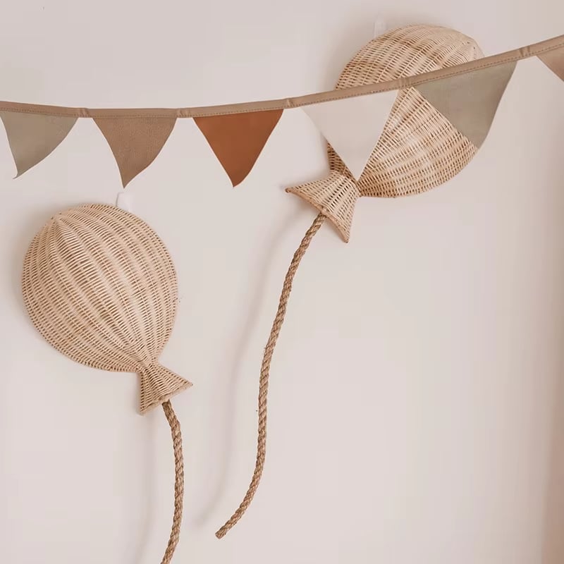 Two hand woven rattan balloons with trailing strings hanging on a wall
