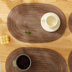 Four oval placemats with a woven straw look in natural tones
