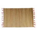 Rectangular hand woven straw placemat with pink cotton tassels at the edges