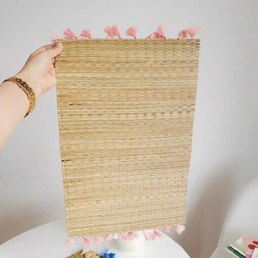 Rectangular hand woven straw placemat with pink cotton tassels at the edges
