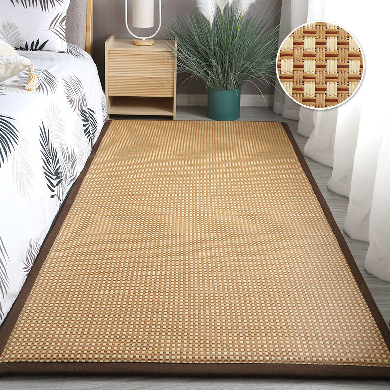 Synthetic rattan rug with a brown border beside a bed