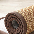 Synthetic rattan rug with a brown border beside a bed