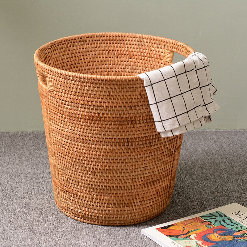 Tall honey rattan laundry basket with a towel draped over the rim