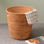 Tall honey rattan laundry basket with a towel draped over the rim
