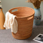 Tall honey rattan laundry basket with a towel draped over the rim
