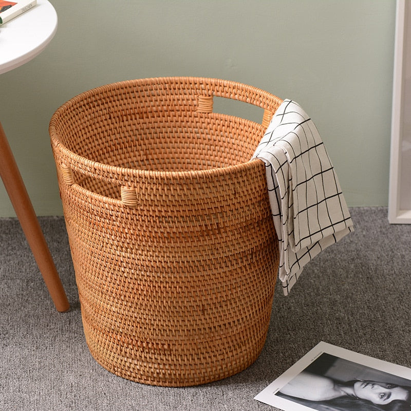 Tall honey rattan laundry basket with a towel draped over the rim