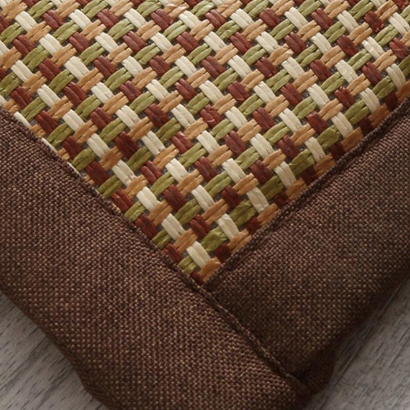 Synthetic rattan rug with a brown border beside a bed