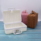 Small white woven rattan box shaped like a retro suitcase with straps