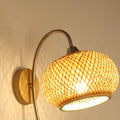 Wall sconce with woven globe shade on a curved metal arm