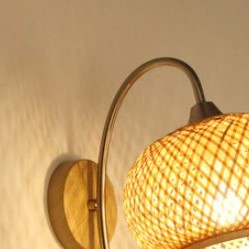 Wall sconce with woven globe shade on a curved metal arm