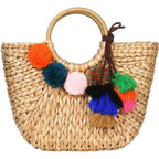 Hand woven basket bag with a round rigid handle and a cascade of colorful pompoms