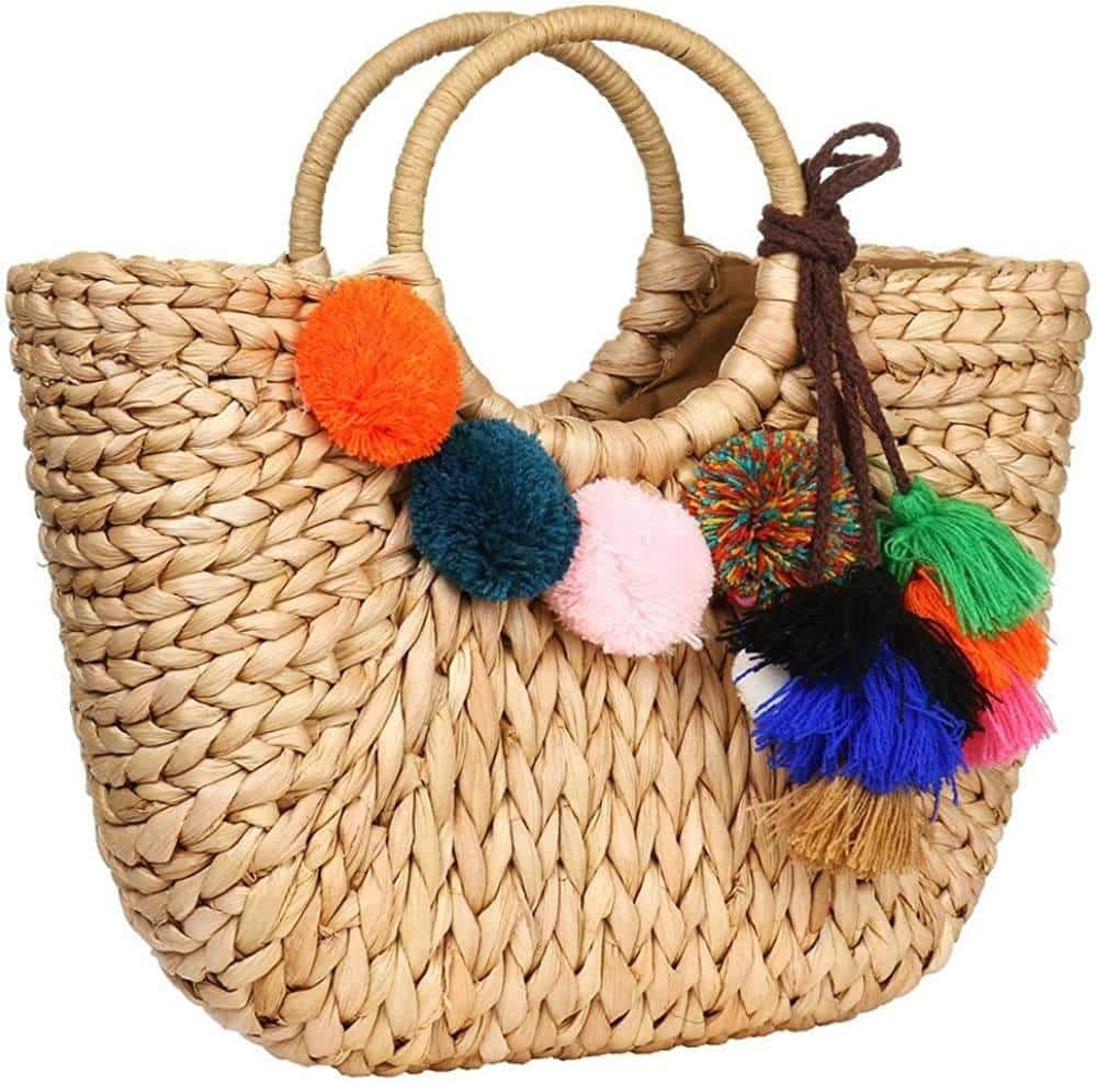 Hand woven basket bag with a round rigid handle and a cascade of colorful pompoms