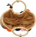 Hand woven basket bag with a round rigid handle and a cascade of colorful pompoms