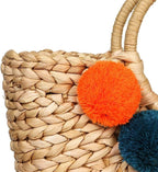 Hand woven basket bag with a round rigid handle and a cascade of colorful pompoms