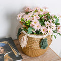 Woven belly basket with green and white tassels holding flowers