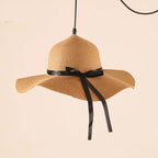 Pendant light shaped like a woven sun hat with black ribbon